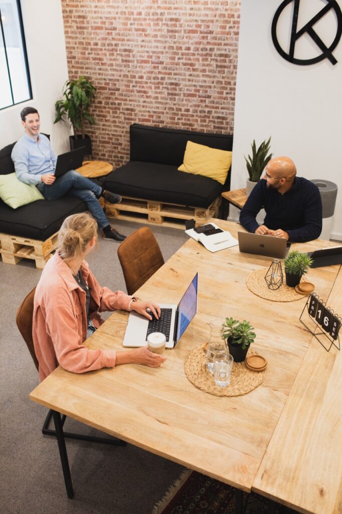 Blick in den Raum mit 3 Coworkern die sich anschauen, Laptop, Lachen